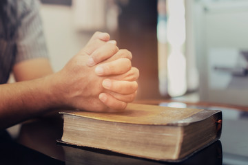 Close up of a man's hands praying on the holy  bible while sitting on a sofa at home