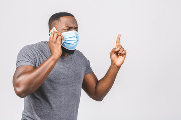 Shocked young african american man in sterile face mask posing isolated on white wall background. Epidemic pandemic coronavirus 2019-ncov sars covid-19 flu virus concept. Using phone.