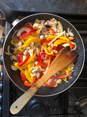 Stir frying chicken, onions and red and yellow peppers in a wok to make fajitas.