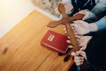 Close up of three Christian people hands holding wooden cross while praying together with the holy...
