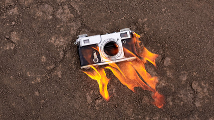 A retro camera burns on dry ground. Fire concept.