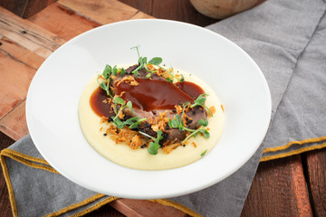Roast beef with mashed potatoes with barbecue sauce on a plate on a wooden background
