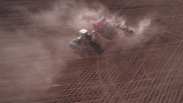View from above, tractor working in a field. Tractor with a seeder, sow crops at field. Sowing agricultural crops. Tractor with a seeder to sowing in a huge field. Agricultural work. Spring sowing