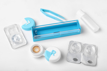Containers with contact lenses, solution and tweezers on white background