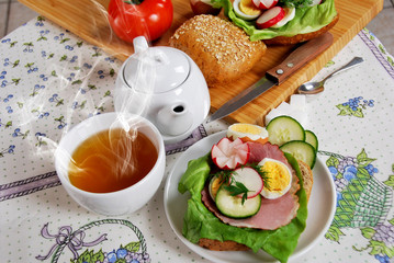 hot tea in a white cup and a ham sandwich
