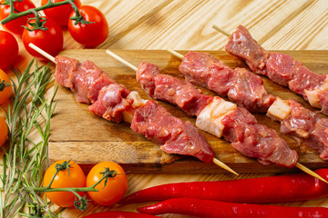 Raw kebab from meat on a wooden background with vegetables.