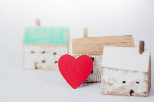 Red heart  lean over wood house model on white background, Conceptual image show love protects and making a happy home