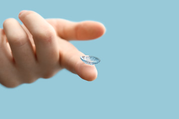 Female hand with contact lens on color background
