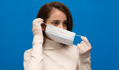 Brown hair girl puts on a mask in white gloves, isolated blue background