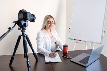 Online education, educational blogging. A young pregnant woman tutor records training video lessons to the camera, she stands and shows with a pen on a flip chart with graphs and diagrams