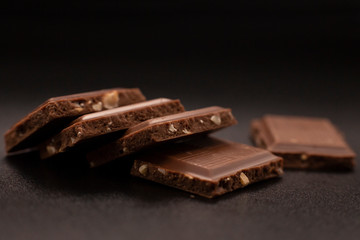 Chocolate with nuts. Chunks of chocolate with nuts on a dark background.