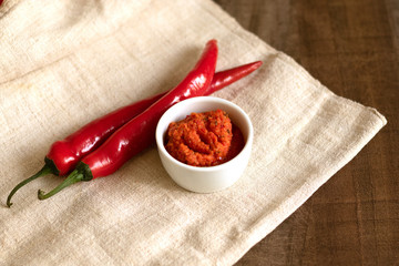 Harissa sauce in the gravy boat. Ingredients for cooking - chili peppers on a linen napkin, on a table