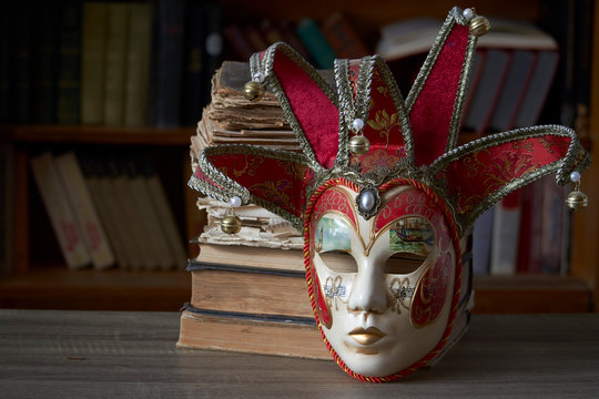 Traditional carnival venetian mask with rich decor on a wooden table in the library, selective focus