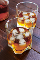 Two glasses of whiskey with ice cubes served on wooden planks.