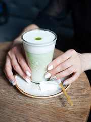 Matcha capucino or green tea latte in vegan cafe with women's hands. Matcha powder. Herbal energy.