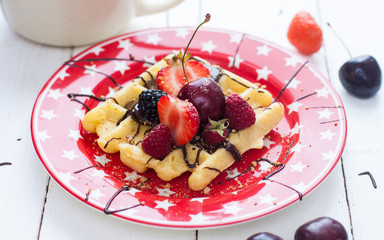 Belgian waffles with strawberry, cherry, blueberry on red plate with stars. White background.