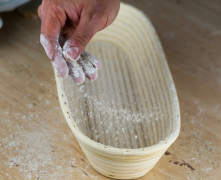 Ein Bäcker bestäubt einen Gärkorb mit Mehl