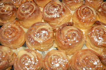 Freshly baked cinnabon buns with cream sauce and cinnamon powder on baking tray. Homemade bakery. Top view. Cinnamon rolls background. 