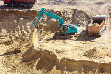 Blue excavator at a construction site working on a pile of sand. The tractor loads the earth into...