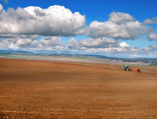 Obraz premium panoramic view of plowed field, tractor with seeder, beautiful sky with clouds. agricultural land, it is time to sow