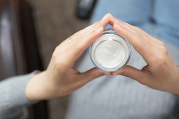 Cropped image of beautiful young woman applying cream while sitting on bed at home