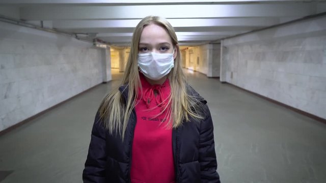 Girl in protective mask goes on crossing where there are no people in public area, underground train subway. infection in public places and transport city. Health isolation and safety quarantine 4k