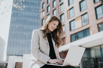 Beautiful lady with laptop and shopping bags, making online orders. Female influencer chat with her friends. Cute smiling teen typing on computer keyboard.