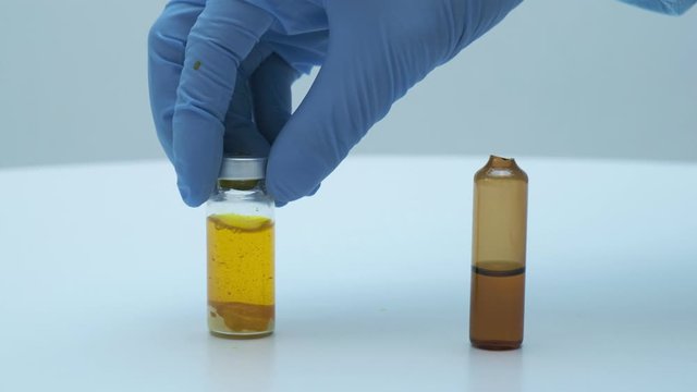 scientist doctor's hands in blue gloves shaking glass phial. yellow liquid and sediment, closeup. preparing vaccine solution for injection. Medicine, healthcare, medical concept, clinic vaccination