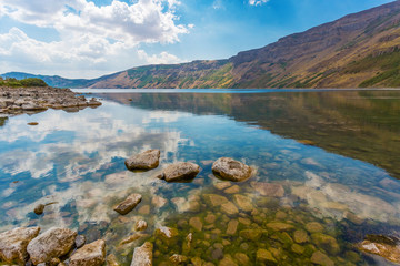 Panoramic view of Ili Lake of Nemrut volcano, Bitlis Province, Eastern Turkey. Mirror water surface. Reflection of the cloudy sky in the lake. Stone bottom through clear water