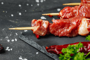 Raw beef kebab with herbs on a dark board, close up