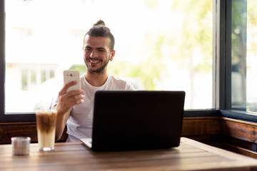 Happy bearded Turkish man with curly hair using phone at the coffee shop