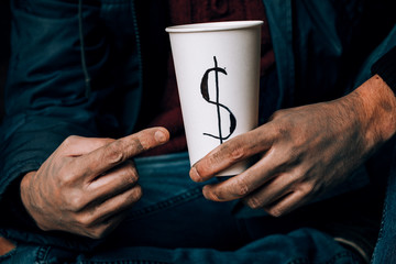 A man begs. He is holding a white paper Cup. The concept of homelessness and poverty.