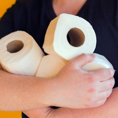 Happy man holds many rolls of toilet paper isolated on a yellow background. Panic due to coronavirus covid-19. Quarantine at home.