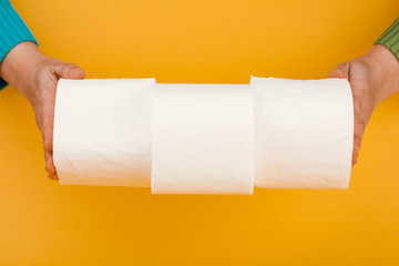 A roll of toilet paper in a woman's hand on a yellow background