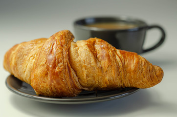 Delicious croissant on a plate with coffee in a cup