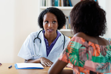 Mature african american female doctor explaining flu and coronavirus symptoms to patient - Powered by Adobe