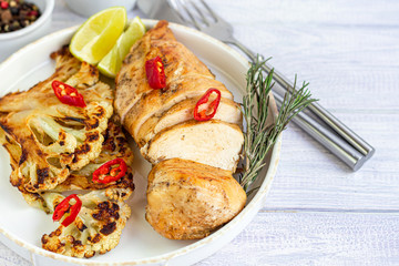 Grilled chicken breast. Near the cauliflower steaks. Garnished with chili peppers and sprigs of rosemary. On a light background.