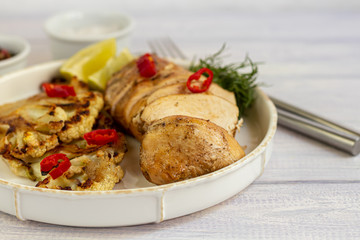 Grilled chicken breast. Near the cauliflower steaks. Garnished with chili peppers and sprigs of rosemary. On a light background.