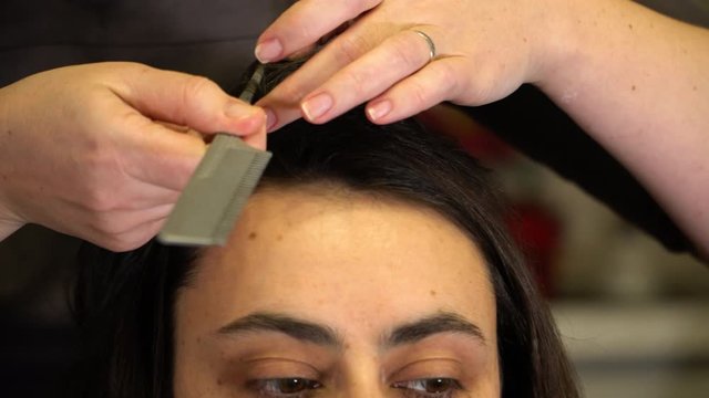 The stylist straightens the strands of a brunette girl's hair and uses a clip