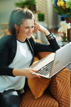 smiling stylish woman using website while sitting on sofa