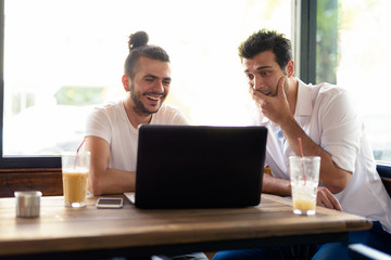 Two happy men as friends using laptop together at the coffee shop