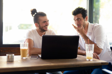 Two happy men as friends using laptop together at the coffee shop