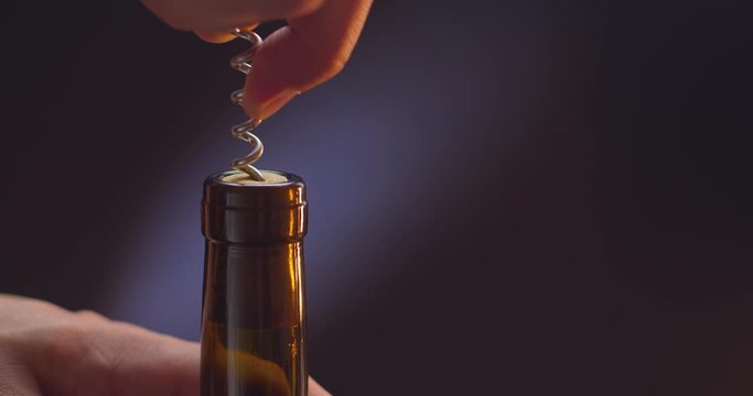 man with a corkscrew opens a bottle of wine on a black background