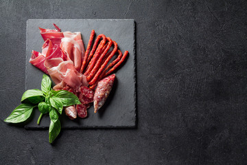 Prosciutto, sausage Fuet and chorizo on a black slate board. Antipasti concept. copy space.