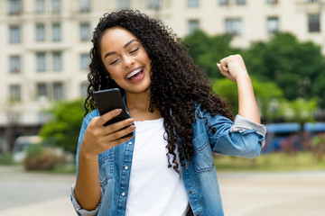 Cheering brazilian young adult woman receiving message with good news on phone