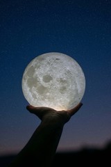 Main tenant la lune devant un ciel étoilé.