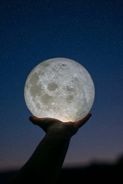 Main tenant la lune devant un ciel &eacute;toil&eacute;.