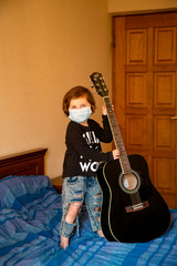 a little girl in a medical mask, and in a rock style, learning to play the guitar, at home during quarantine, due to the covid-19 pandemic