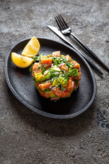 Salmon avocado salad served with culinary ring on black plate