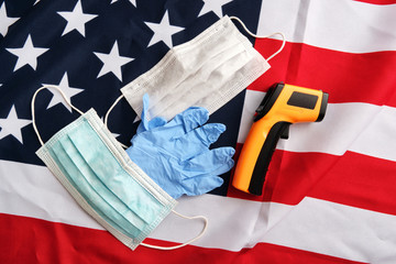 Used protective face masks, gloves, non-contact infrared thermometer on american flag background. Covid-19 quarantine. Flat lay, top view